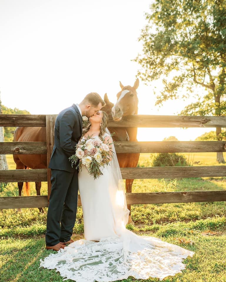 bride and groom kissing in front of fence with horses